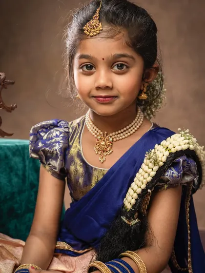 A close-up portrait of a girl in a traditional blue silk lehenga, her hair adorned with 'moggina jade'. Her direct gaze is captivating.