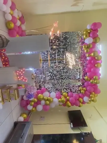 A home birthday party setup with a silver shimmer wall. The decor features a pink, white, and gold balloon garland and marquee numbers.