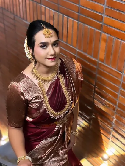 This Muhurtham look is all about effortless glow. The focus is on beautiful skin, with a soft smokey eye and a deep red lip that complements the rich maroon saree and traditional gold jewellery.
