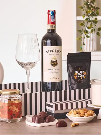 Perfect for a wine-loving couple, this hamper includes a bottle of red wine, a witty "I wine a lot" glass, gourmet bar snacks, and chocolates, all presented in a stylish striped box.