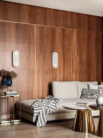 Another angle of the wood-paneled living room, showing the modern wall sconces that provide soft, ambient light. The mix of textures, from the wood wall to the soft throw and metallic tables, adds depth and interest.