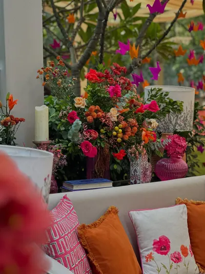 A vibrant lounge area from a "Pigment Paradise" themed event, with colorful printed cushions, bright floral arrangements, and hanging origami birds.