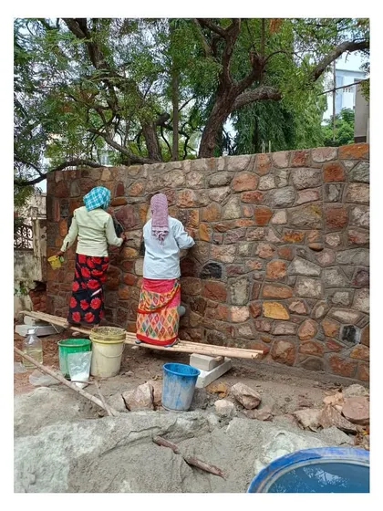 Local craftswomen clean and point the random rubble masonry wall, bringing their own unique style and fondness for the hardy local material.