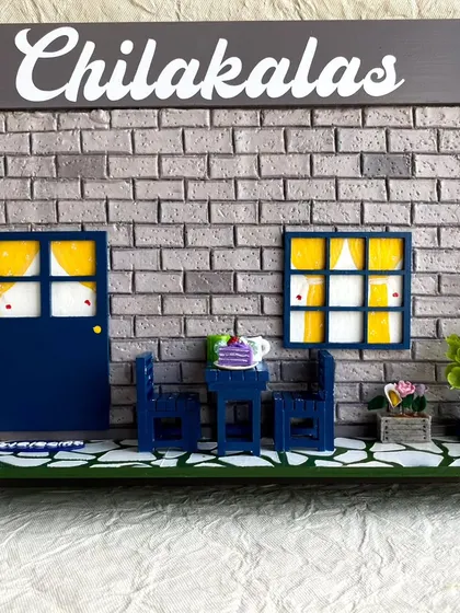 I designed this miniature nameplate for the 'Chilakalas' family, featuring a cozy outdoor scene. The design includes a hand-textured brick wall, a miniature door and window with curtains, and tiny furniture.