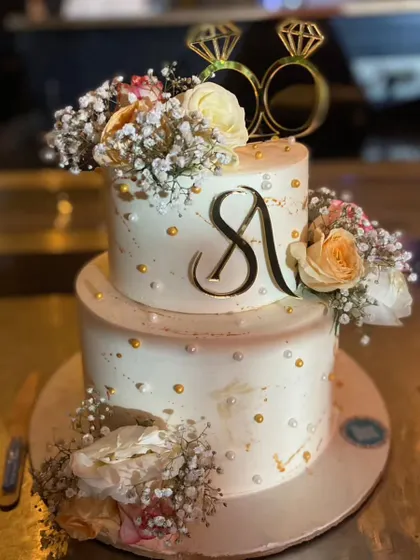 A classic two-tier engagement cake with a monogram and fresh floral arrangements. The design is simple yet sophisticated, making it a timeless choice for any celebration of love.