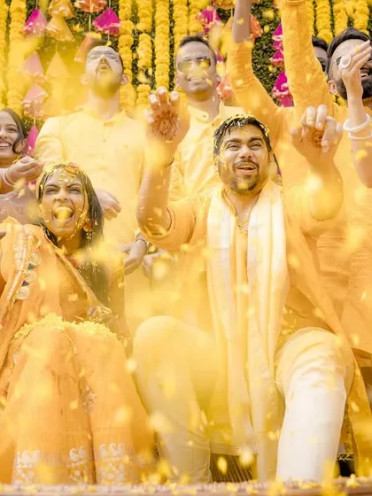 A high-energy moment from a Haldi ceremony, with the couple and their friends cheering as they are showered with flower petals.