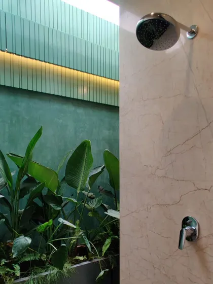 A detail of the shower, with a fluted green wall, marble, and lush plants creating a rich textural and color palette.