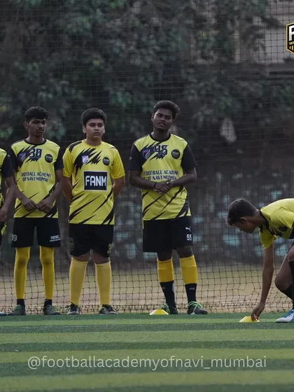Players watch intently as a teammate sets up cones for the next drill. This shows the focus and readiness of the team before a practice session.