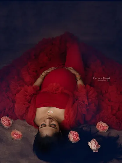 A creative top-down shot creating a heart shape with the dramatic red gown. This artistic angle offers a unique and memorable maternity portrait.