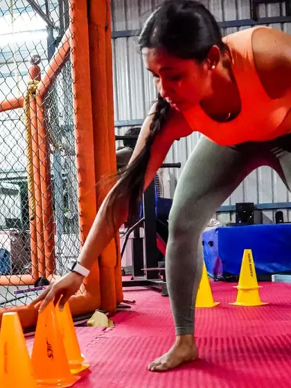 A female member works on agility drills with cones inside the cage. Our training is about more than just fighting; it's about building complete athletic fitness.