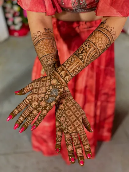 A bridal mehendi with personalized initials "S" and "G" set against a backdrop of a red lehenga.
