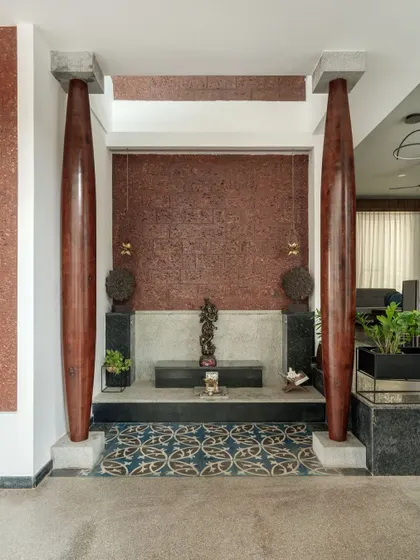 The Pooja space is designed as a serene, open-to-sky niche. Flanked by two traditional wooden pillars against a textured laterite wall, it feels both contemporary and deeply rooted in local architectural traditions.