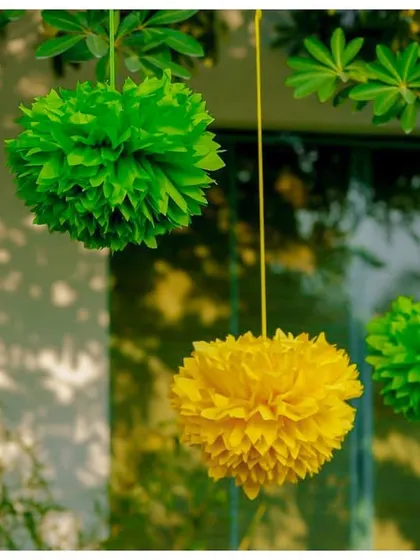 Colourful paper pom-poms in yellow and green hang from a tree, adding to the festive and cheerful atmosphere of the outdoor party.