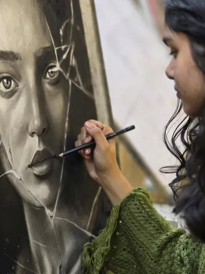 A close-up shot of an artist carefully drawing the cracks on a piece of shattered glass in her hyper-realistic charcoal portrait.