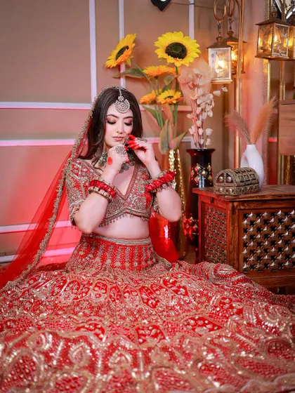 A full-length seated portrait showcasing a heavily embroidered red lehenga.