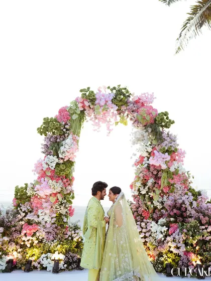 A quiet moment for the couple under the lush floral arch, composed of pink, white, and green blooms, just before their Varmala ceremony.