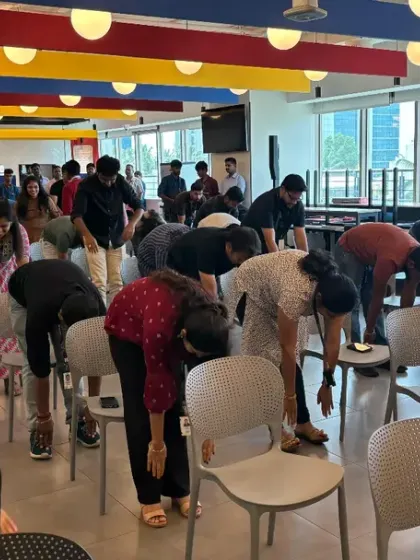 Employees engage in a forward bend using chairs for support, a perfect stretch to release lower back tension caused by sitting.