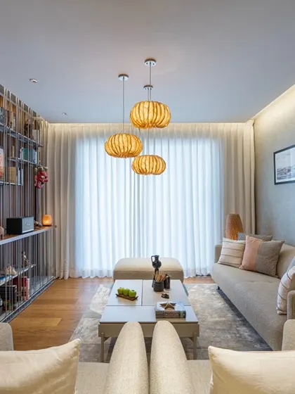 This living room showcases a harmonious blend of textures, from the fluted wood wall panels to the soft, earthy tones of the furnishings. Pendant lights made from banana fiber cast a warm, inviting glow over the space.