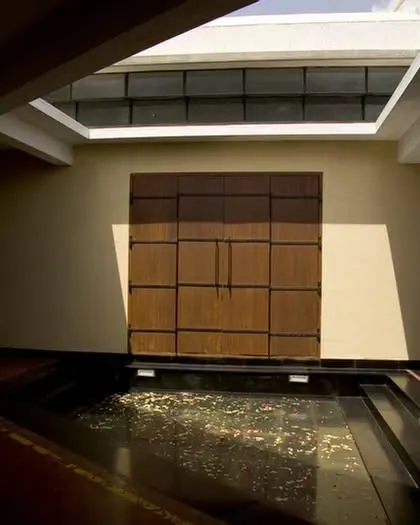 An internal courtyard at the Synergy Textiles Factory features a water body and a large wooden panel, creating a cool microclimate and a serene pause point for workers. A skylight above brings in natural light, enhancing the sense of tranquility.