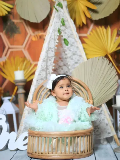 A boho-themed milestone shoot for a one-year-old. The setup includes a lace teepee, dried palm leaves, and a rustic wicker chair.