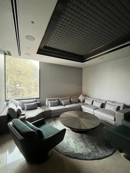 An example of our Art Deco inspired interiors, this room features a custom grey sectional sofa and green swivel armchairs. The most striking feature is the quilted ceiling panel, a unique design element that adds texture and a sense of bespoke luxury.
