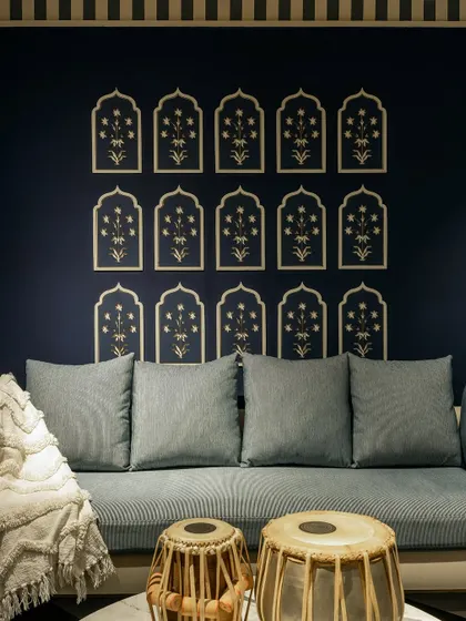 A custom-built seating area with a light blue upholstered bench set against a deep navy wall. The wall is adorned with traditional Indian block print motifs, and the space is accessorized with tablas, reflecting a blend of modern and cultural design.