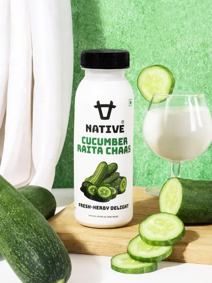 This shot for a cucumber raita chaas drink uses a fresh, green color palette and natural styling. The composition with fresh cucumbers and a filled glass highlights the natural ingredients and refreshing taste.