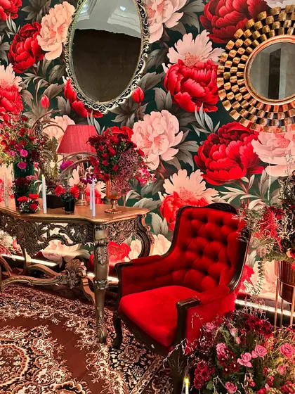 A vintage-inspired photo booth with a bold floral wallpaper, a red velvet royal chair, and ornate mirrors, creating a perfect spot for glamorous pictures.