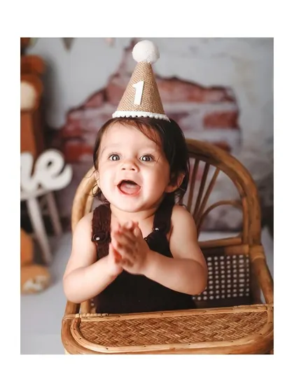A happy birthday boy clapping his hands, wearing a '1' party hat in a rustic, bear-themed setup.