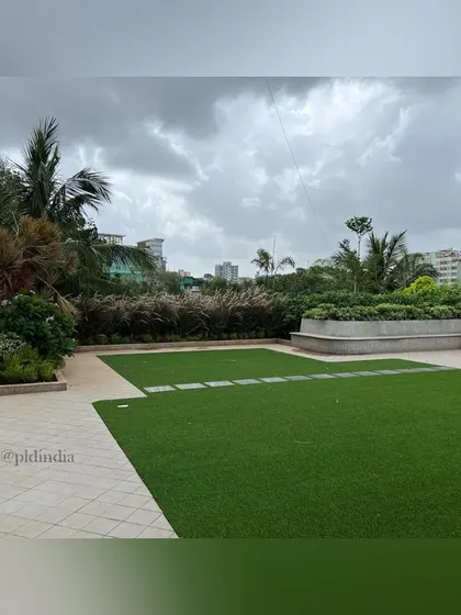 This wide shot showcases the expansive lawn area, designed for corporate events and employee recreation. The space is framed by raised planters filled with ornamental grasses and trees, providing a natural boundary and visual interest.