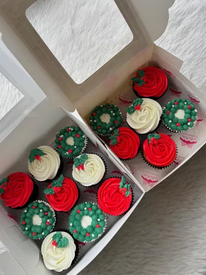 A box of assorted Christmas cupcakes, combining the wreath design with simple red and white frosted ones topped with a holly leaf. Perfect for holiday gifting.