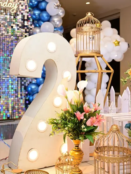 A light-up number '2' used as a prop for a second birthday party. It's paired with elegant floral arrangements and decorative birdcages.