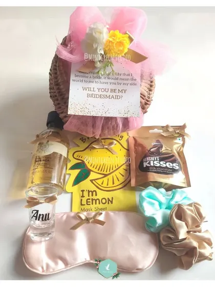 A perfect way to ask, "Will you be my bridesmaid?" This proposal hamper is packed in a rustic basket and filled with pampering items like a face mask, a personalized shot glass, a silk eye mask, and chocolates.