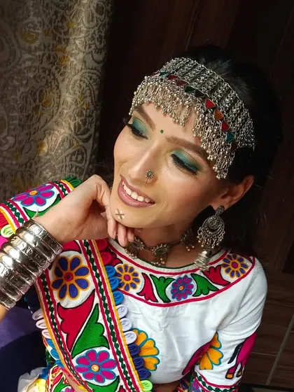 A smiling portrait of a model ready for Garba. The look features green eyeshadow, oxidized silver jewelry, and a traditional 'bandhani' outfit.