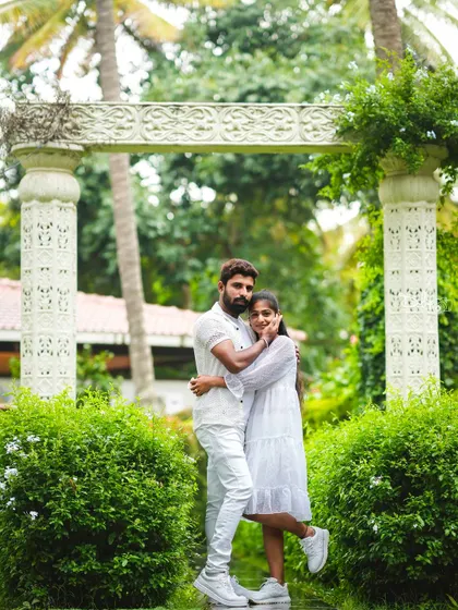 A romantic portrait in front of a white stone archway, surrounded by lush greenery.