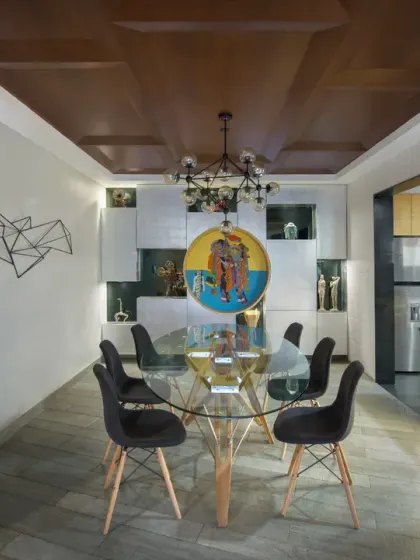 The modern open kitchen in the Grey Apartment flows into the dining area, allowing easy interaction. The dining space is defined by a glass-top table, a custom chandelier, and a feature wall displaying curated art.