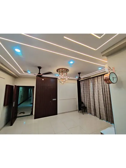 This image highlights a modern false ceiling design with integrated LED strip lighting and a central chandelier. This layered lighting approach allows for creating different moods in the same room.