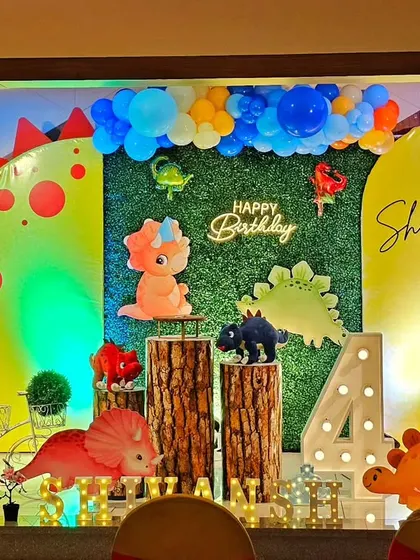 A colorful and friendly dinosaur-themed party for a 4th birthday. The setup features cute dinosaur cutouts, a greenery backdrop, and a light-up marquee number.