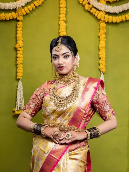 The full view of the bride against a traditional floral backdrop. The jewellery, from the maang tikka to the waist belt, creates a complete and stunning picture.