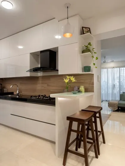 A look at one of our custom modular kitchen solutions. This design features sleek, handleless white cabinets, a contrasting wooden backsplash, and a practical breakfast bar, creating an open and inviting culinary space that is perfect for modern living.