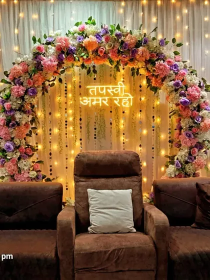 An elegant backdrop for a Jain Tapasvi ceremony. I used a beautiful arch of pastel flowers, a custom neon sign with the blessing "Tapasvi Amar Raho," and warm lighting to create a serene and respectful setting in the family's home.