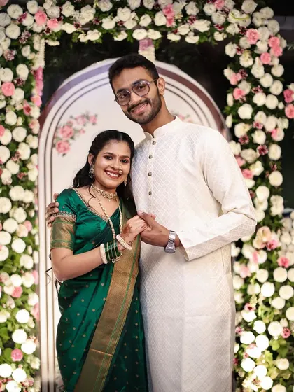 A happy portrait of an engaged couple holding hands in front of a floral archway.