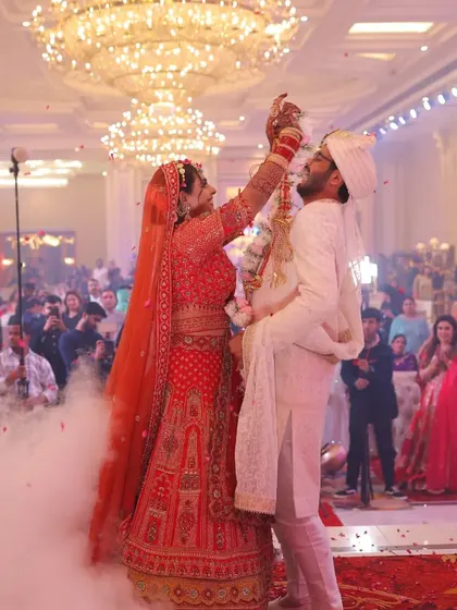 The bride joyfully places the varmala on the groom in a grand hall filled with guests, surrounded by a cloud of low-lying fog for a dramatic effect.