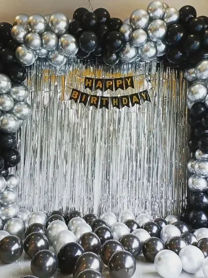 A simple yet classic birthday backdrop with a silver shimmer curtain and a black and silver balloon arch.