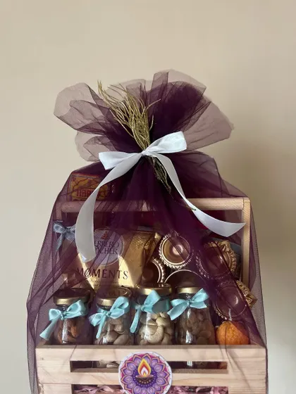 The wooden crate Diwali hamper wrapped in purple tulle, viewed from the side.