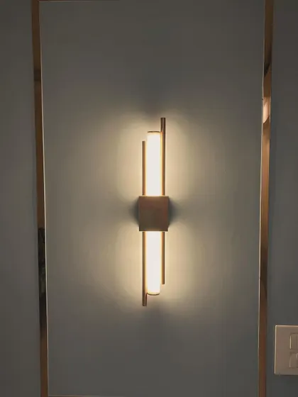 This modern wall sconce is a perfect example of accent lighting. Set against a cool grey wall with a metallic gold frame, it not only illuminates the space but also acts as a piece of sculptural art, adding a touch of elegance.