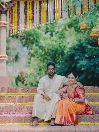 A formal portrait of the couple, showcasing the rich colors of their traditional South Indian wedding attire against the rustic backdrop.
