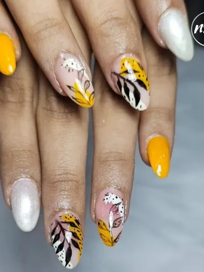 A sunny and cheerful set of hand-painted nails. The combination of solid yellow, pearl white, and a leafy pattern with animal print accents is perfect for a summer look.