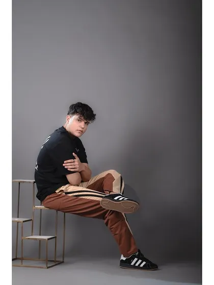 A full-length shot of a model in a casual, streetwear-inspired outfit. The use of a simple prop and a solid grey background keeps the focus squarely on the clothing and sneakers.