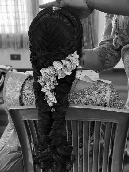 A black and white shot capturing a quiet moment of styling. The focus is on the intricate details of the braid and the placement of the flowers.